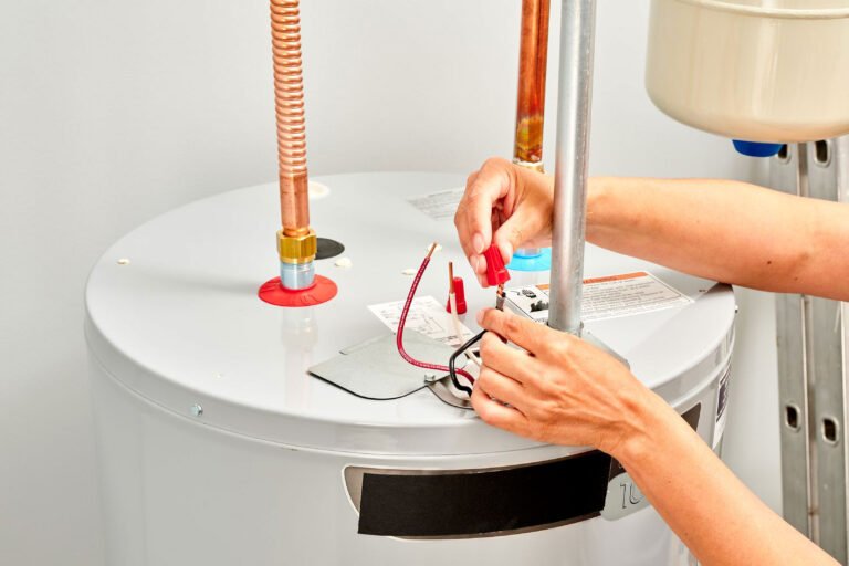 Technicien raccordant des fils électriques sur un chauffe-eau avec tuyaux en cuivre.