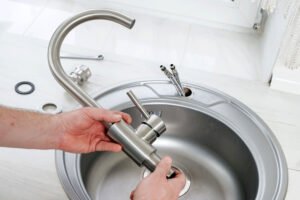 Plombier installant un robinet en acier inoxydable sur un évier rond en métal.