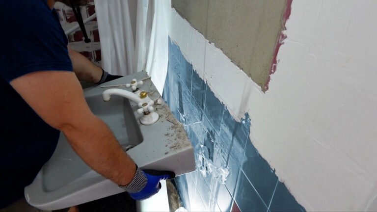 Plombier retirant un lavabo mural ancien lors d'une rénovation de salle de bain.